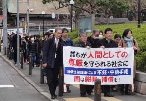 「誰もが人間としての尊厳を守られる社会に　旧優生保護法による不妊・中絶手術　国は謝罪と補償を　のスローガンの書かれた横断幕を持って歩く、原告・弁護団・支援者たち