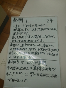 ホワイトボードに書かれた文字。「2年生　事例１　まだだれもいないのに邪魔といい、入れてあげないのは差別だから、出入りのしやすい場所に「どうぞ」と言ってあげればよかった。事例２　差別ではないが、席までは介助者が行き、タダで入れてあげる。（介助）終わったらまた介助者を呼べばいいのではないか。事例３　マニュアルが差別　その店の上の人に「車椅子でも大丈夫か」と聞いたほうがよかったのではないか」