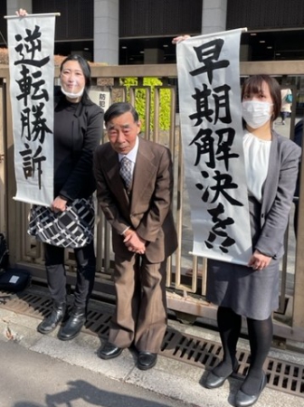 応援にお礼する原告の北三郎さん（中央）。弁護団が「逆転勝訴」「早期解決を」を書かれた紙を掲げている
