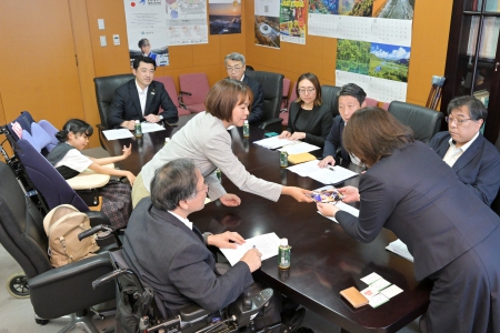 スキー合宿の写真を吉竹さんが政務官に見てもらっている様子