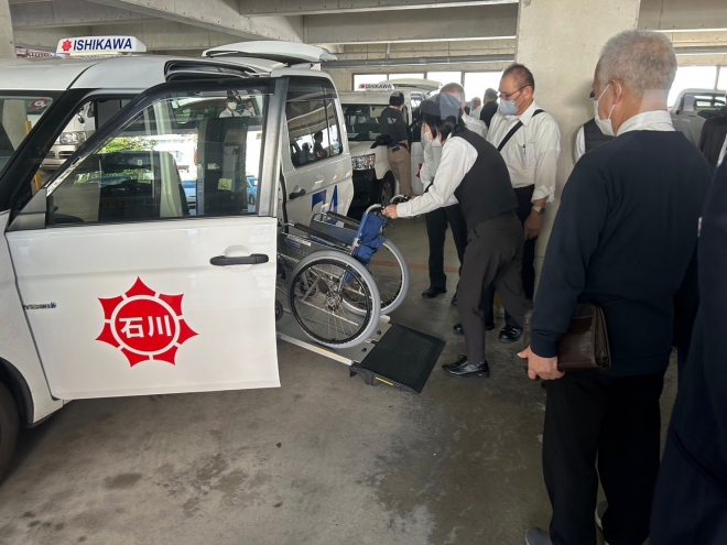 手動車いすを使ってタクシーへの乗車練習を乗務員がする様子